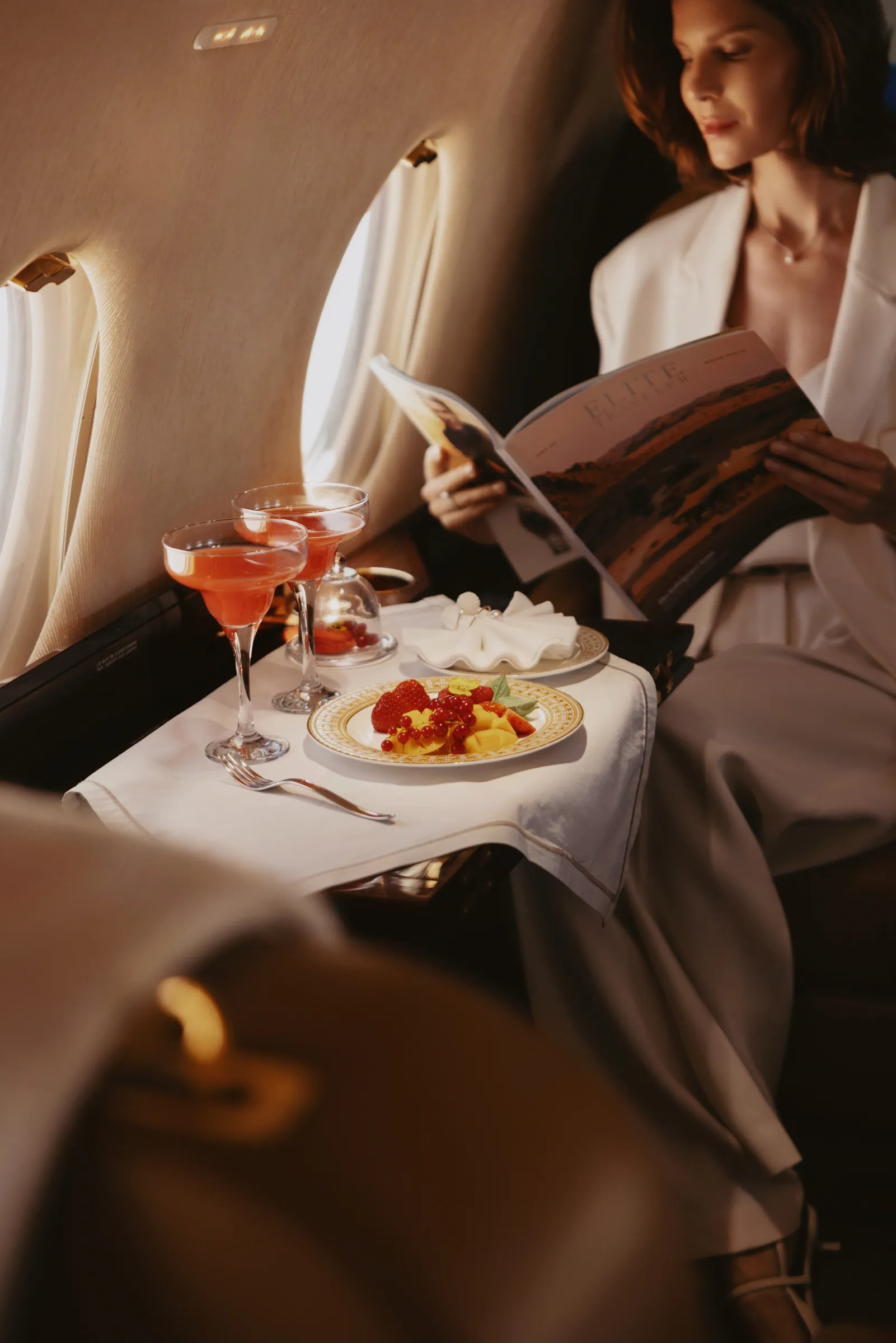 A guest reading beside a table with cocktails and fruit in the Gulfstream G200 cabin